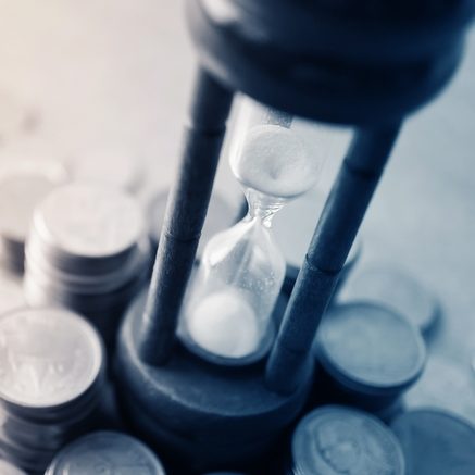 Sablier au centre de pièces de monnaie, symbolisant le temps et l'argent.